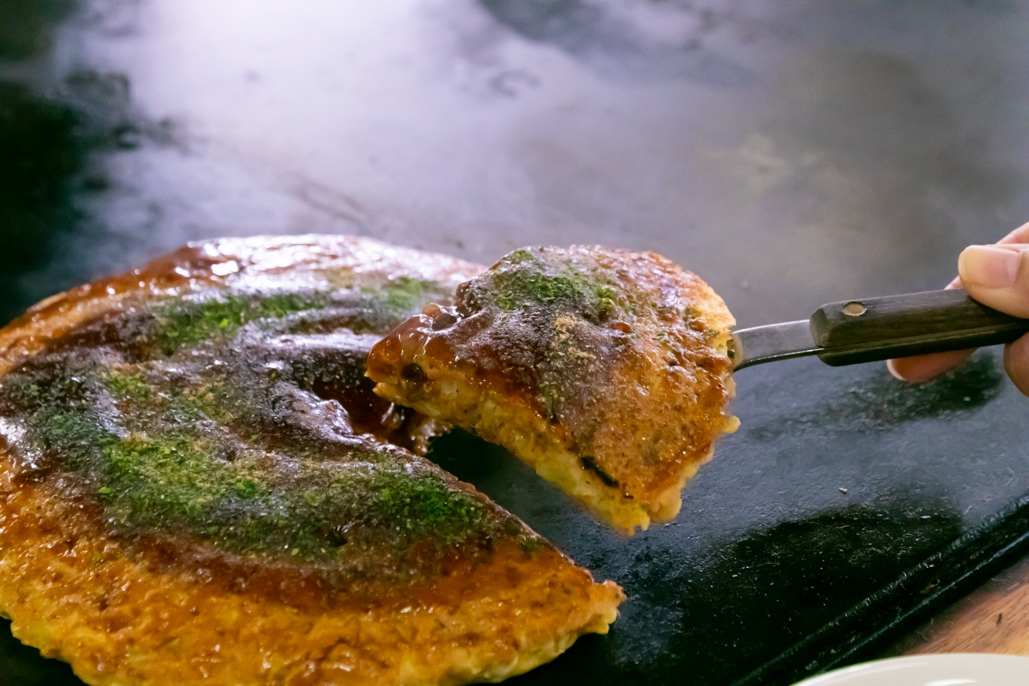 画像：げんちゃんのお好み焼きをヘラで持ち上げている様子